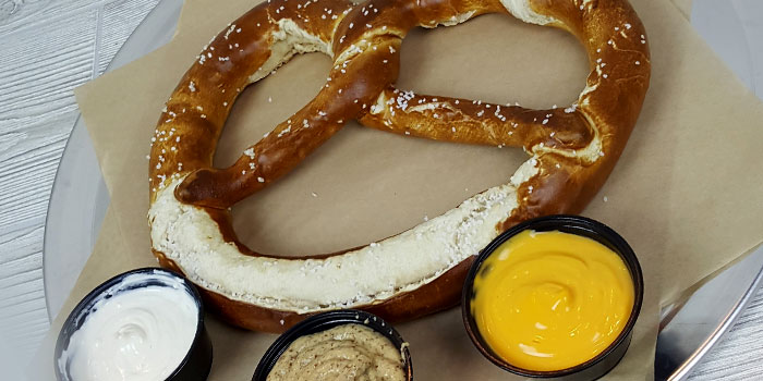 Jumbo hot pretzel from the appetizer menu served at Chippewa Falls Bowl with side cups of nacho cheese and mustard dipping sauces